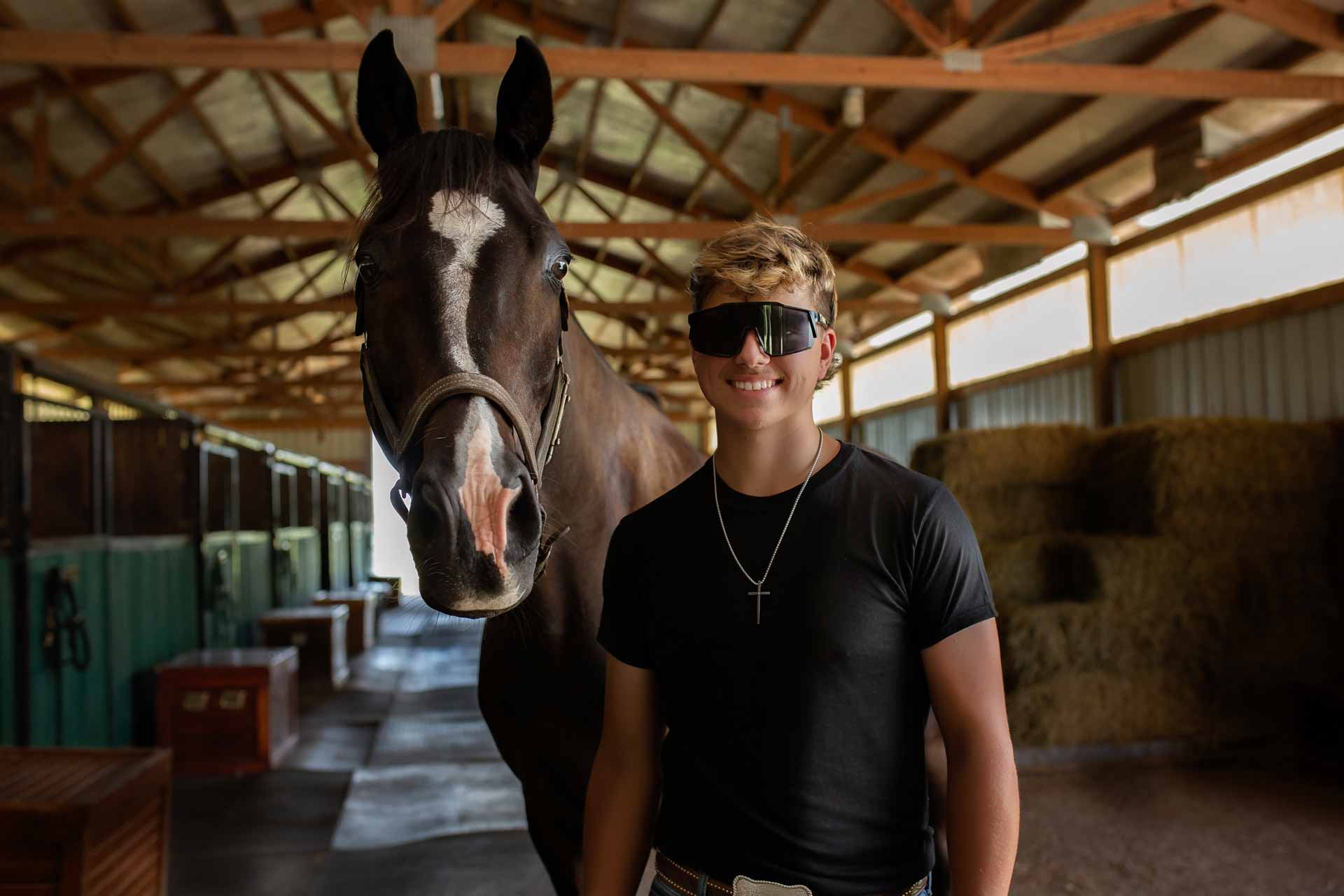 Teenage boy standing in the barn with his horse staring at the camera during professional photography session at Moments By T Franklin Tennessee