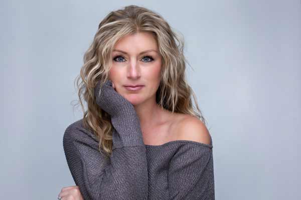 A blonde woman with curls in her hair wearing a gray off the shoulder sweater. With one hand on her cheek. photoshoot at Romantic Moments By T in Franklin TN 
