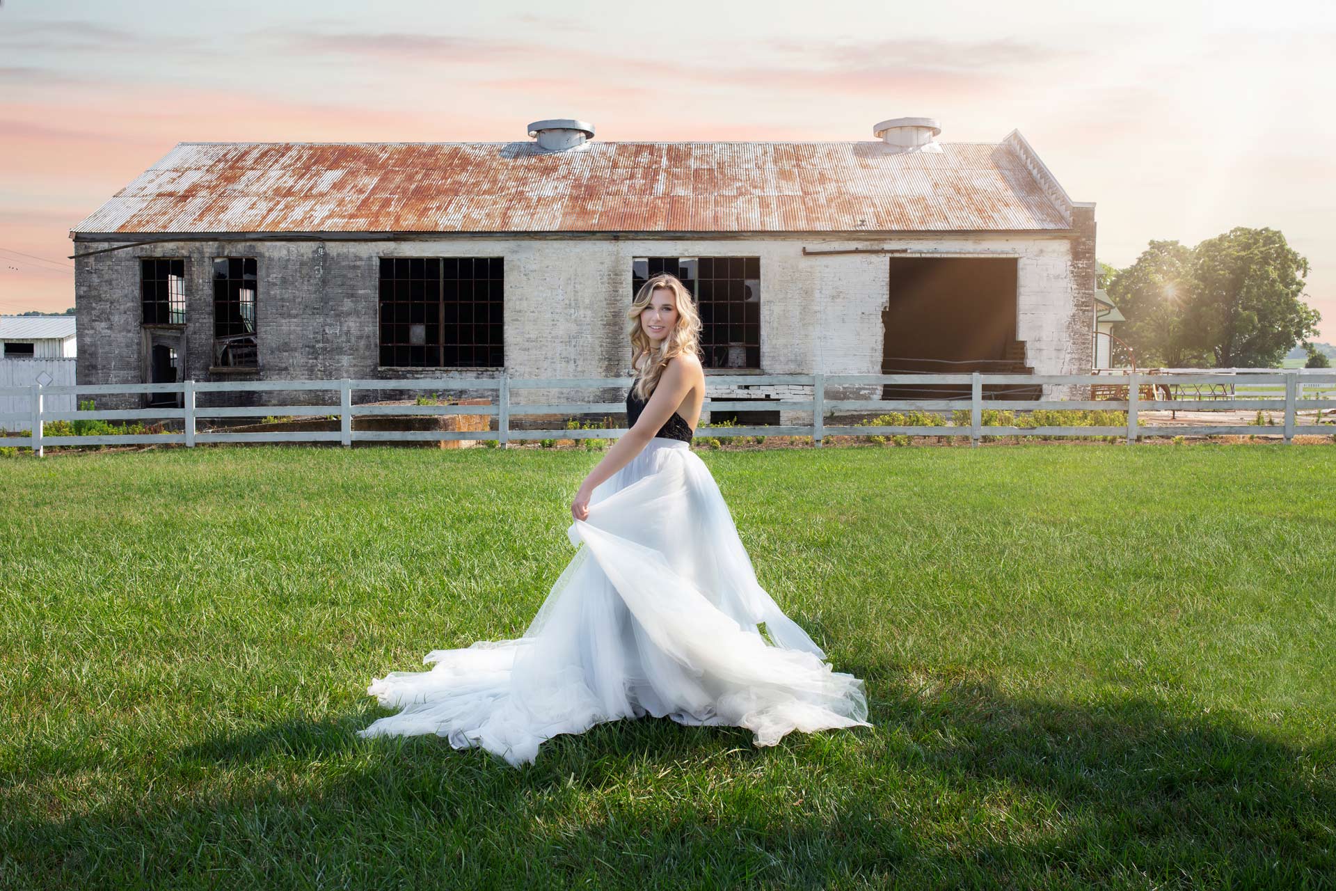 high school senior girl wearing a long tulle skirt and dancing on the grass in front of a rustic barn during a professional senior photography session at Moments By T, Franklin Tennessee