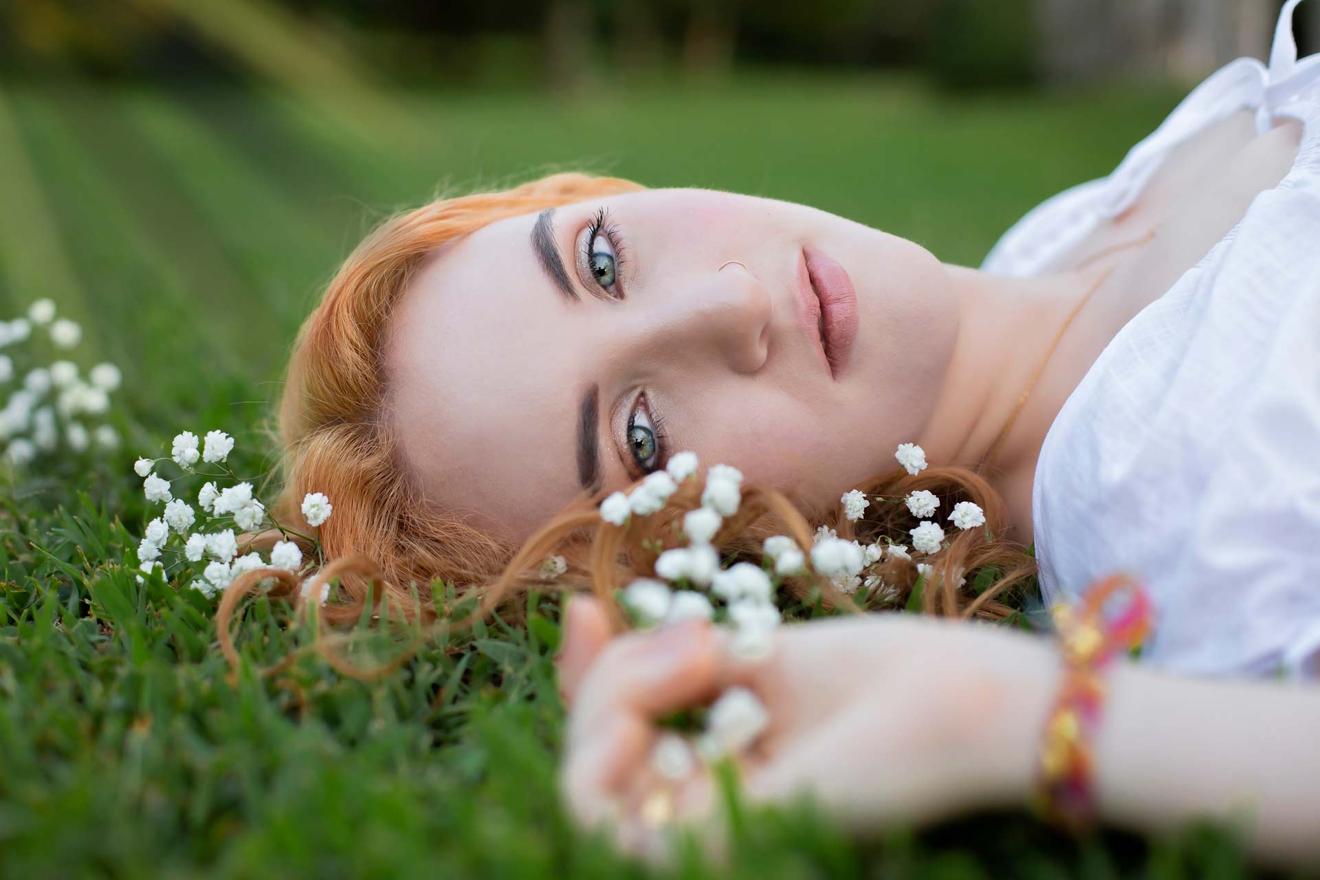 Redhead high school senior laying on the grass with flowers around her during professional senior photography session at Moments By T, Franklin Tennessee