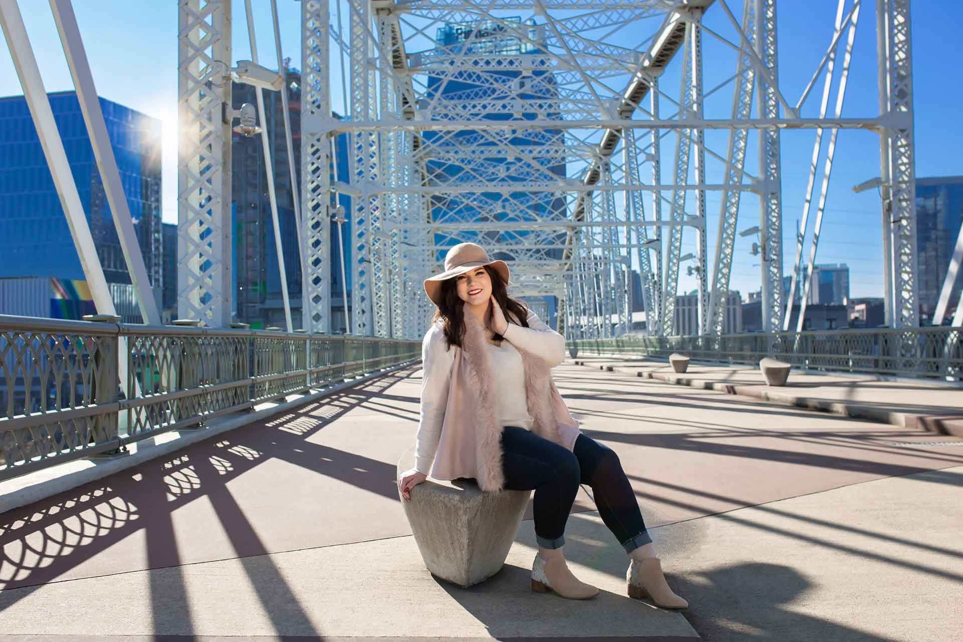 High school senior girl sitting on the Nashville pedestrian bridge during a professional senior photography session at Moments By T, Franklin Tennessee