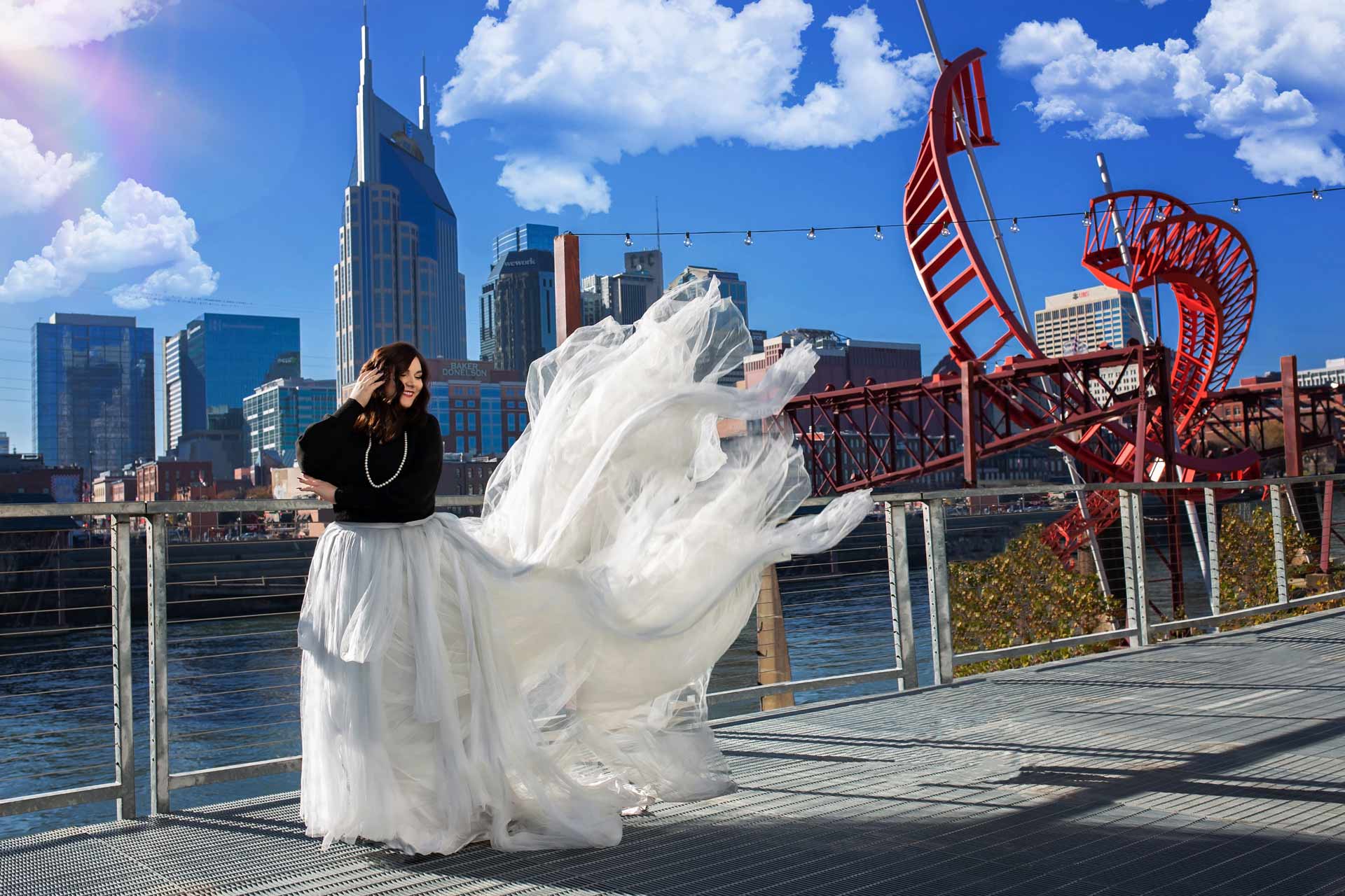 High school senior wearing a long flowy tulle skirt in downtown nashville with the skyline behind her during a professional senior photography session at Moments By T, Franklin Tennessee
