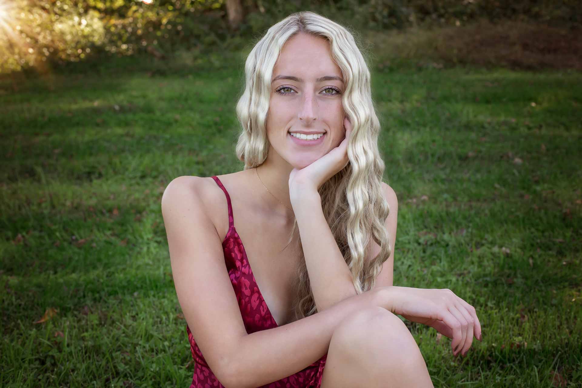 Blonde senior girl sitting on the grass posing during a professional senior photography session at Moments By T, Franklin Tennessee
