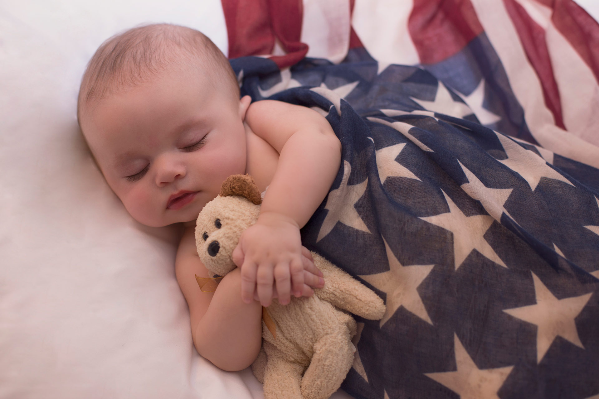 Newborn baby wrapped in American flag during patriotic themed portrait session at Moments By T Photography Studio Franklin Tennessee